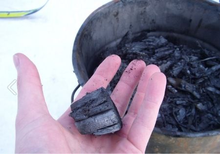 Mano sujetando un trozo de carbón vegetal, biochar.