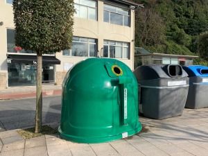 contenedor verde de ecovidrio al lado de otros conteneodores de reciclaje en una calle