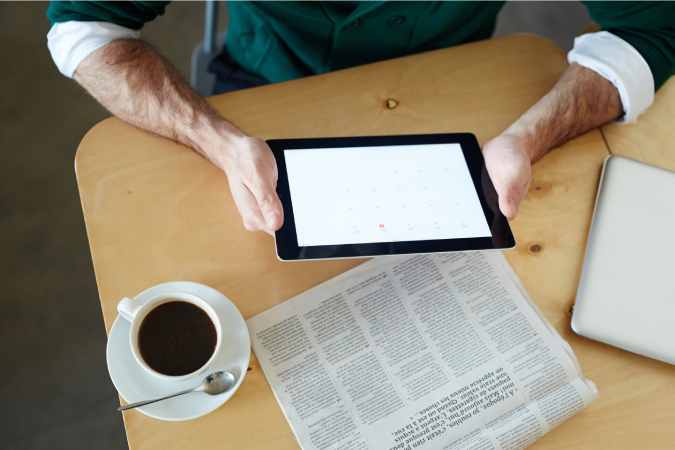 persona leyendo noticias en una tablet y el periódico
