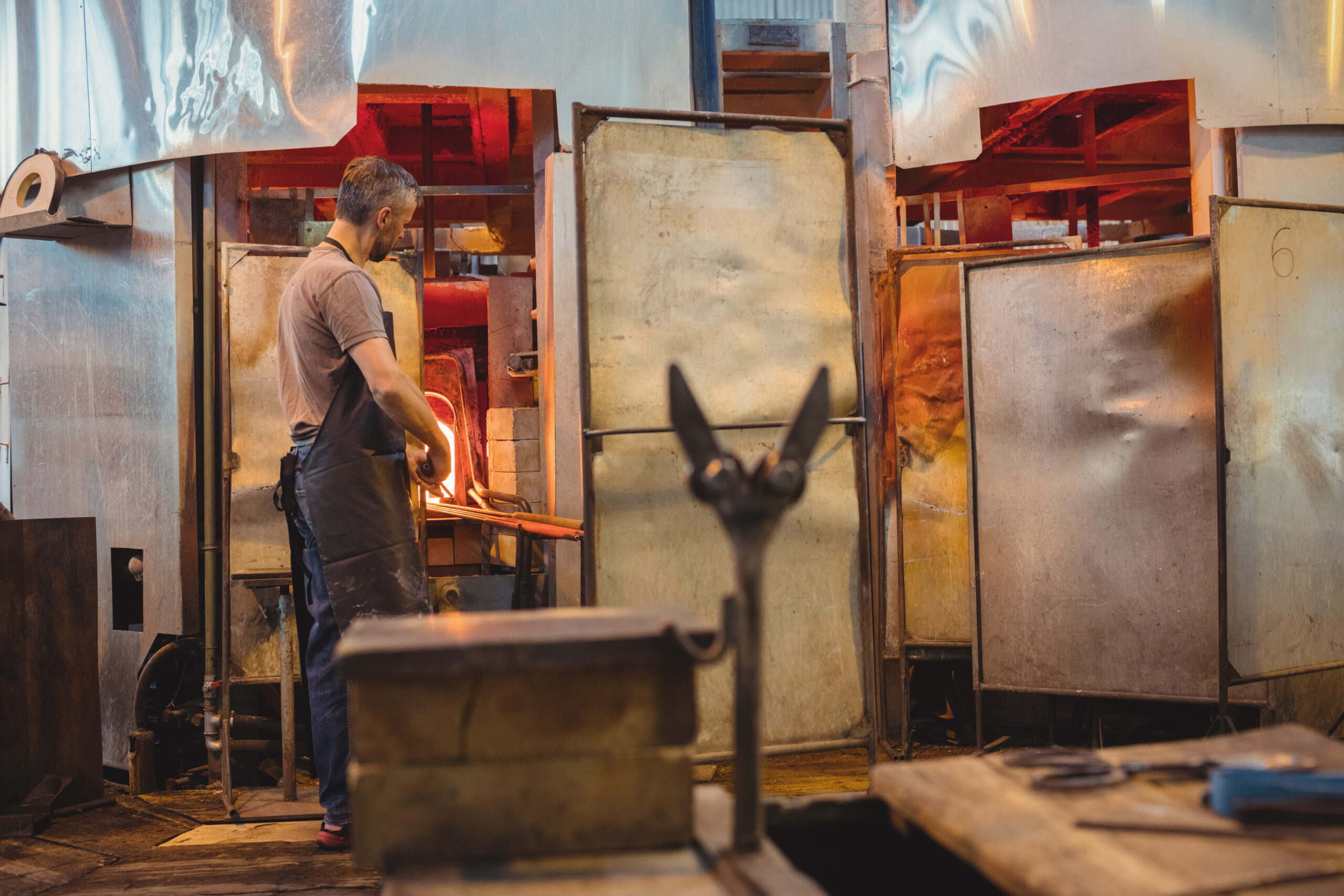 Operario trabajando frente a un horno industrial de alta temperatura durante el proceso de fabricación del vidrio, utilizando herramientas especializadas
