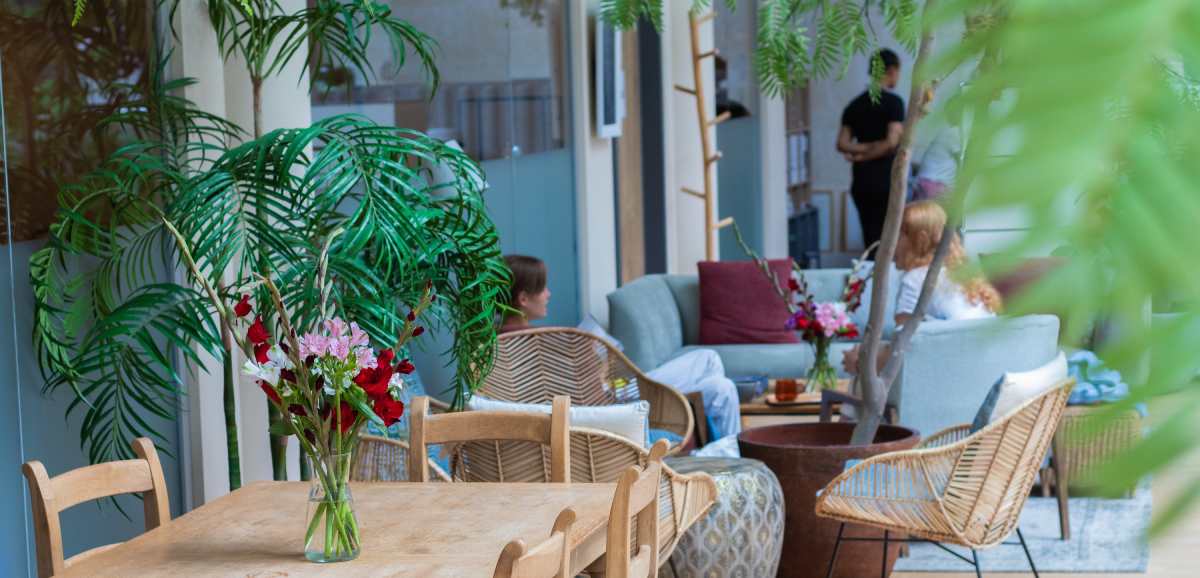 espacio público interior en el que poder descansar. Aparecen mesas y sillas, sillones al fondo con vegetación
